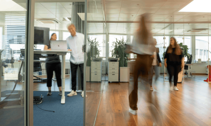Büroszene mit mehreren Mitarbeitenden, die sich im Büro bewegen und sich austauschen.