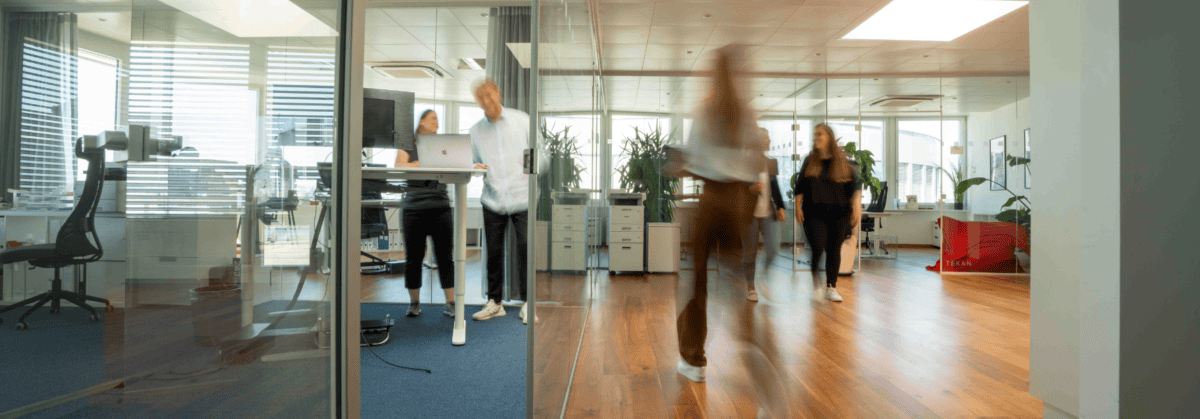 Büroszene mit mehreren Mitarbeitenden, die sich im Büro bewegen und sich austauschen.