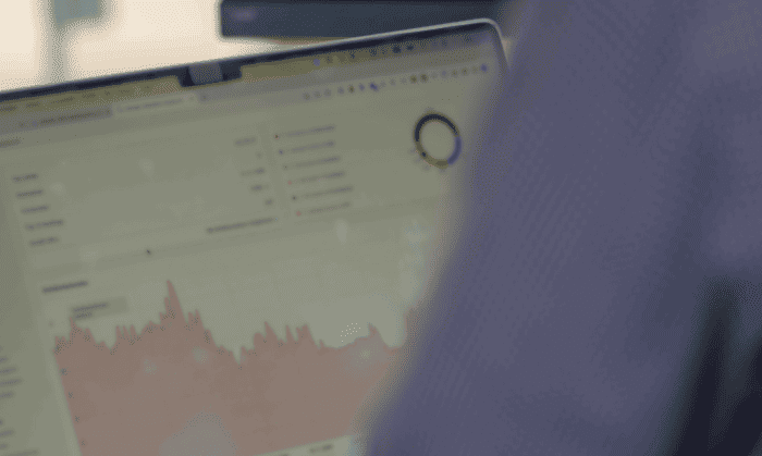 Eine Person arbeitet an einem Laptop, auf dessen Bildschirm ein Dashboard mit Diagrammen und Statistiken zu sehen