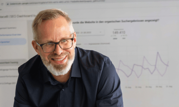 Bruno während einer Besprechung. Im Hintergrund ist ein grosser Bildschirm mit Diagrammen und Statistiken.