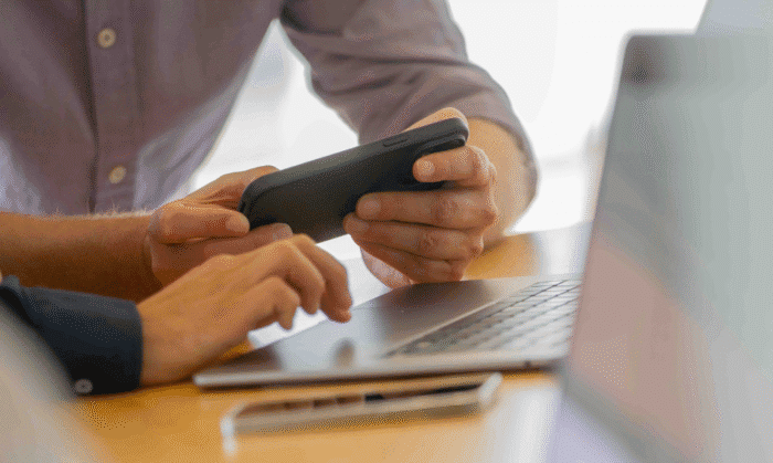 Eine Person hält ein Handy in der Hand und die andere Person ist am Laptop.