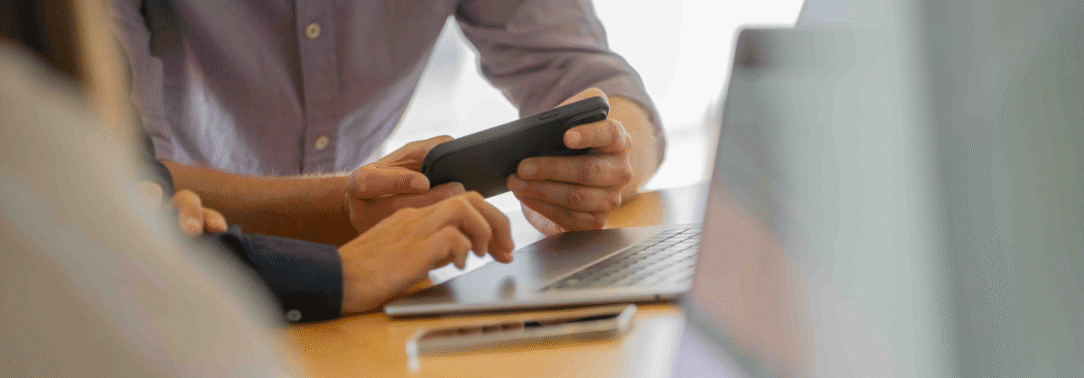 Eine Person hält ein Handy in der Hand und die andere Person ist am Laptop.